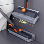 Two wall-mounted cleaning brushes with long handles are shown in a bathroom-like corner with a 27 cm dimension marker. The product appears to be a pair of gray and orange adhesive brush cleaners.