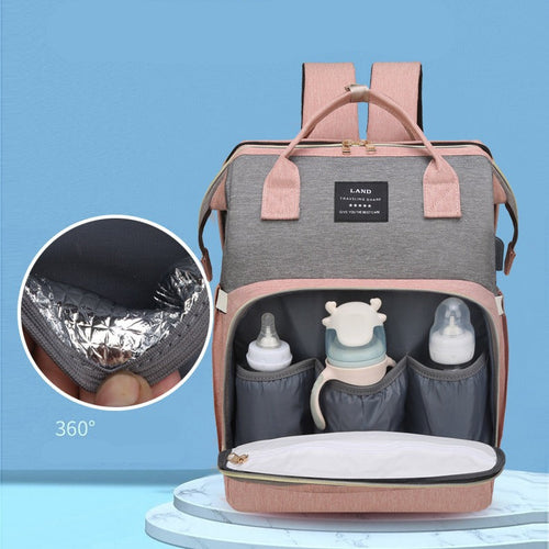 A pink and gray diaper backpack shown open on a light blue background, with three front bottle holders, a diaper pocket, and an inset circle highlighting the insulated lining.